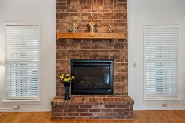 interior details with wood finished floors, a brick fireplace, and baseboards