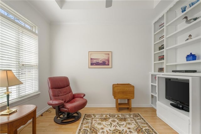 living area featuring light wood-style flooring, baseboards, and crown molding