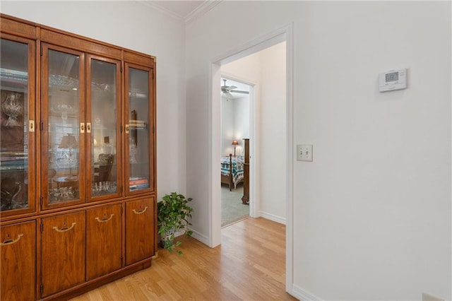 hallway featuring light wood-style flooring, baseboards, and ornamental molding