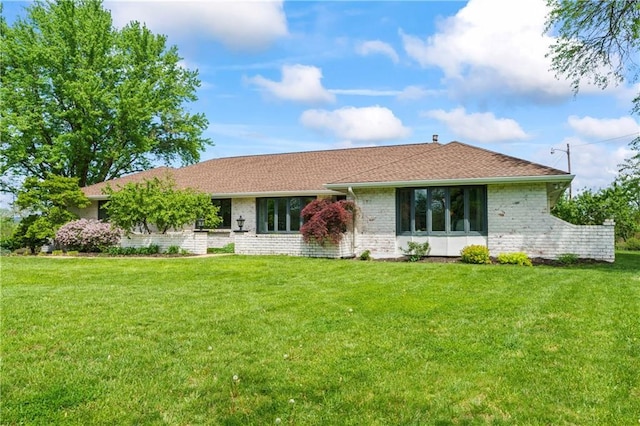 view of front of house with a shingled roof, a front lawn, and brick siding