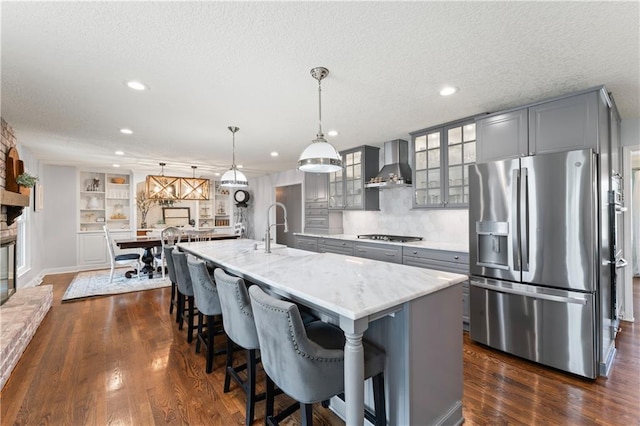 kitchen with wall chimney range hood, a textured ceiling, gray cabinetry, a sink, and stainless steel appliances