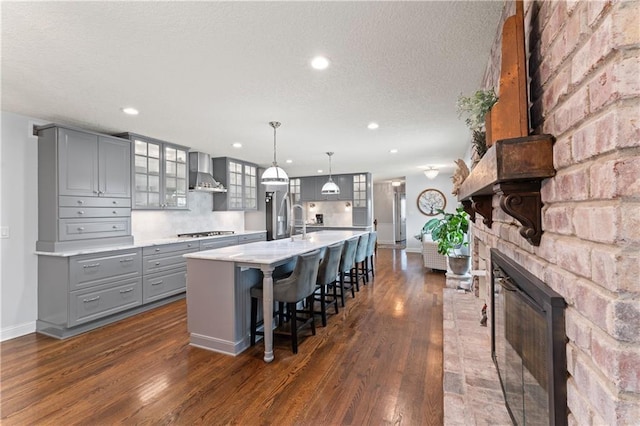 kitchen featuring wall chimney range hood, gray cabinets, dark wood finished floors, light countertops, and stainless steel gas stovetop