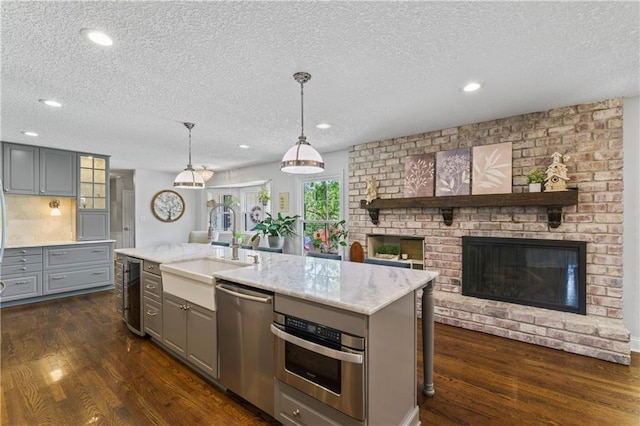 kitchen with gray cabinets, a textured ceiling, appliances with stainless steel finishes, a brick fireplace, and wine cooler