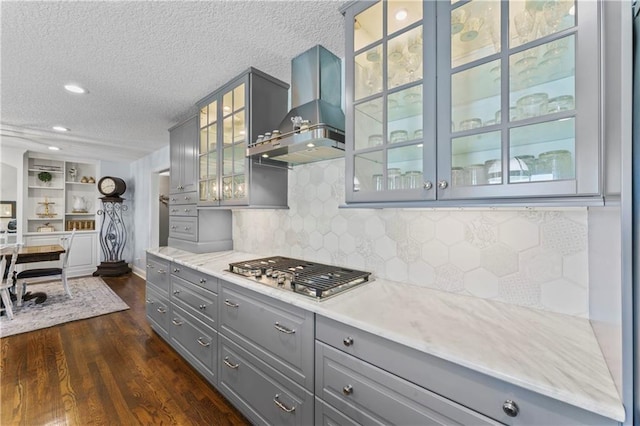 kitchen with stainless steel gas cooktop, a textured ceiling, wall chimney exhaust hood, dark wood finished floors, and gray cabinetry