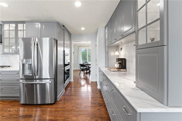 kitchen featuring a textured ceiling, stainless steel appliances, backsplash, gray cabinetry, and dark wood-style floors