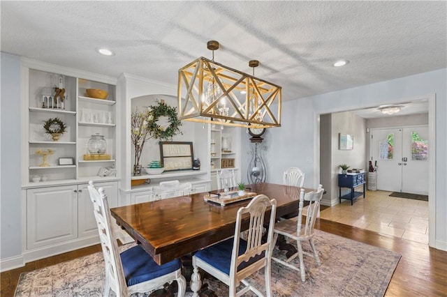 dining area featuring a textured ceiling, an inviting chandelier, built in features, and wood finished floors