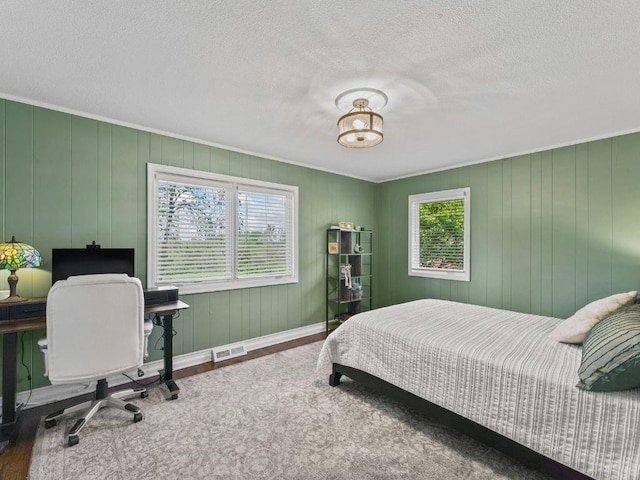 bedroom featuring a textured ceiling, visible vents, crown molding, wood finished floors, and baseboards