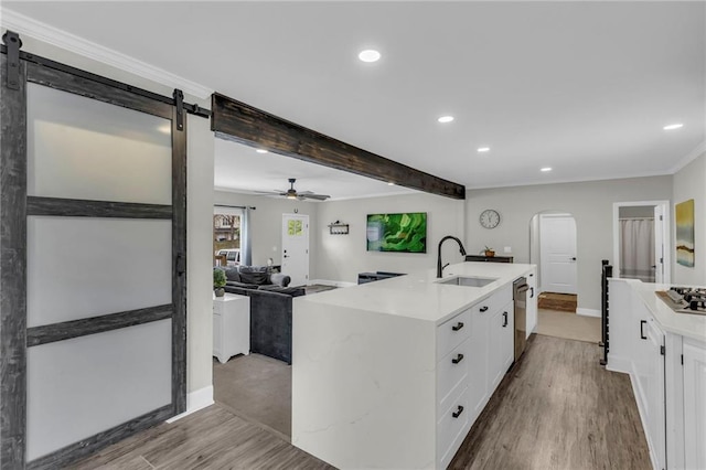 kitchen with a sink, arched walkways, wood finished floors, white cabinets, and recessed lighting