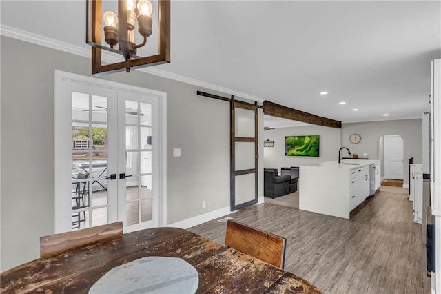 living area with arched walkways, a barn door, french doors, ornamental molding, and wood finished floors
