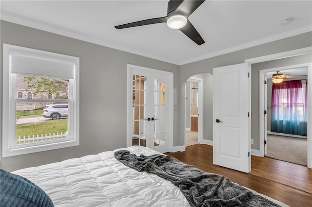 bedroom with arched walkways, ornamental molding, wood finished floors, french doors, and a ceiling fan