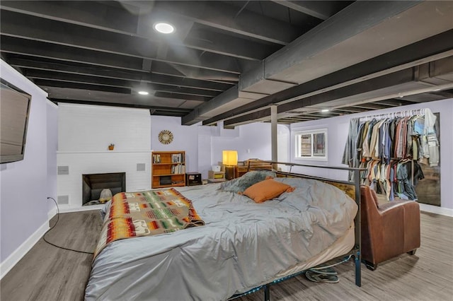 bedroom featuring wood finished floors, baseboards, and a brick fireplace