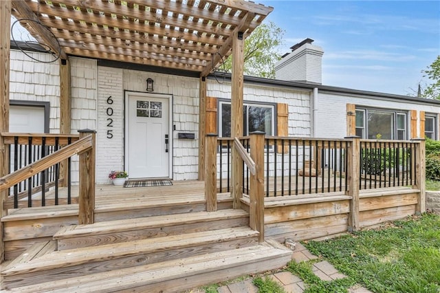 view of exterior entry featuring brick siding, a chimney, a pergola, and a deck