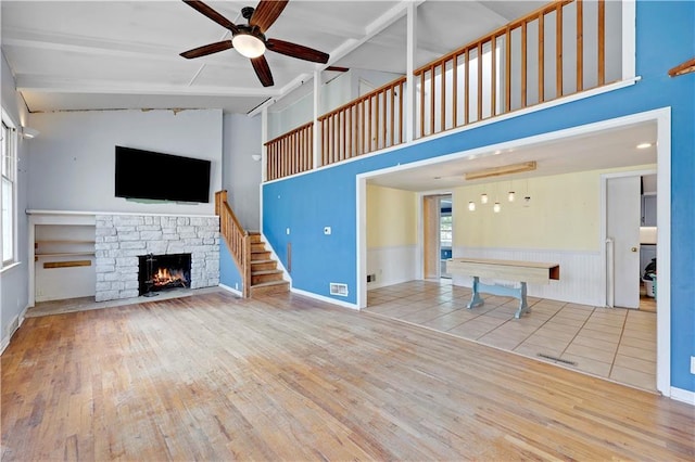 unfurnished living room featuring a ceiling fan, wood-type flooring, beamed ceiling, a fireplace, and high vaulted ceiling