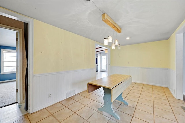 unfurnished dining area featuring a wainscoted wall, visible vents, and light tile patterned floors