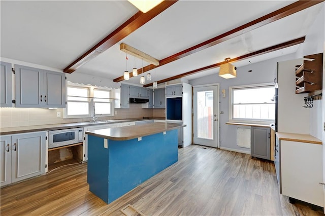 kitchen with light wood-style flooring, beam ceiling, tasteful backsplash, white microwave, and under cabinet range hood