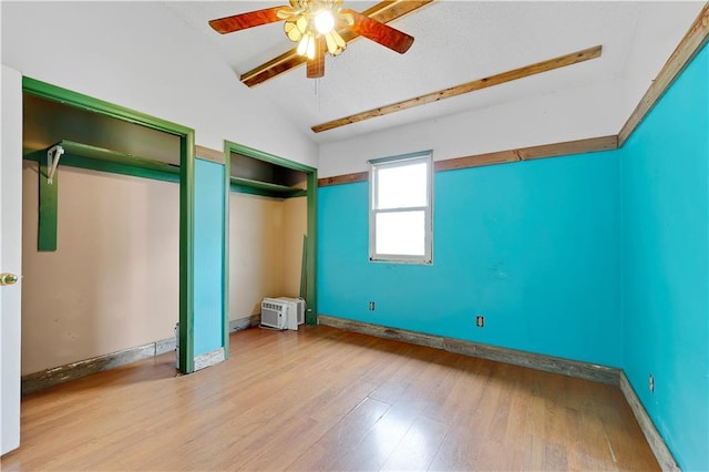 unfurnished bedroom with vaulted ceiling, wood finished floors, baseboards, two closets, and ceiling fan