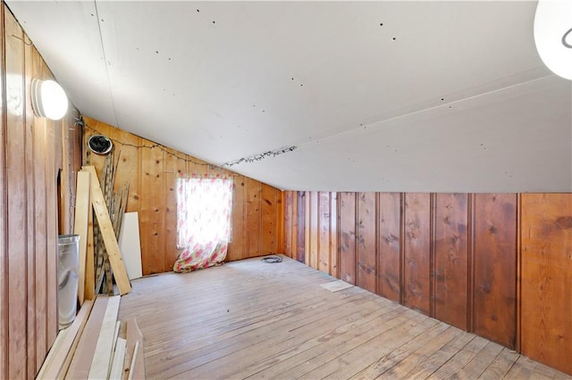 bonus room featuring lofted ceiling, wooden walls, and light wood-style floors