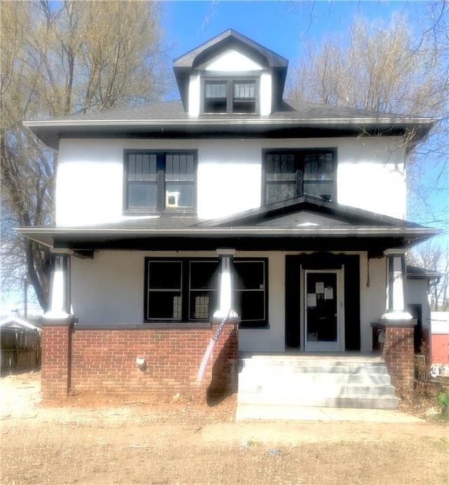american foursquare style home featuring stucco siding, covered porch, and brick siding