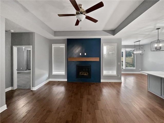 unfurnished living room featuring dark wood-style flooring, ceiling fan with notable chandelier, baseboards, and a fireplace