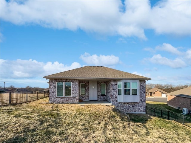 rear view of property featuring brick siding, fence private yard, a shingled roof, and a lawn