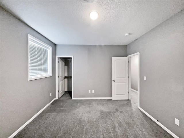 unfurnished bedroom featuring a closet, carpet flooring, a textured ceiling, baseboards, and a spacious closet