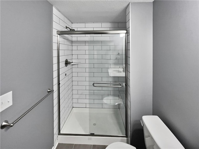 bathroom with toilet, a textured ceiling, and a shower stall