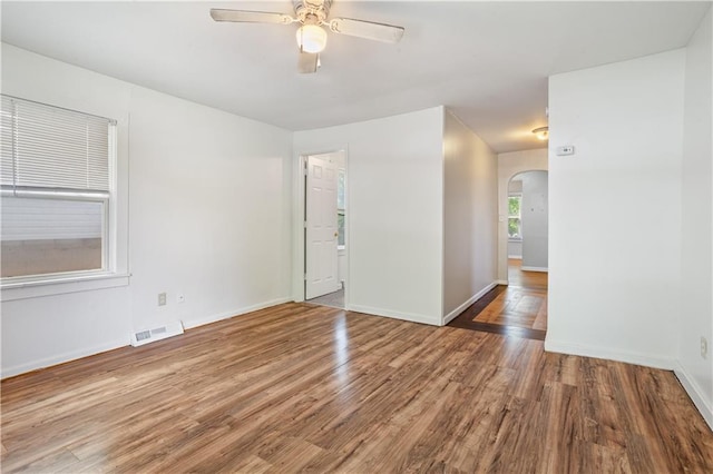 empty room with wood finished floors, a ceiling fan, visible vents, baseboards, and arched walkways