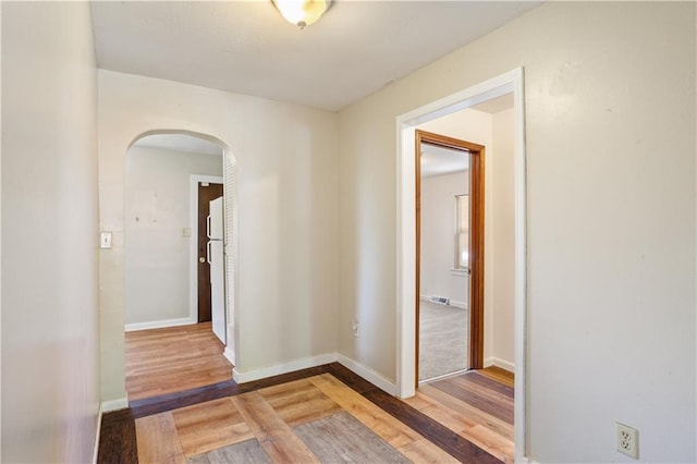 hall featuring arched walkways, light wood-type flooring, and baseboards