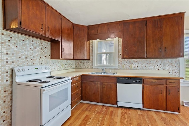 kitchen with a sink, white appliances, light countertops, light wood-style floors, and decorative backsplash