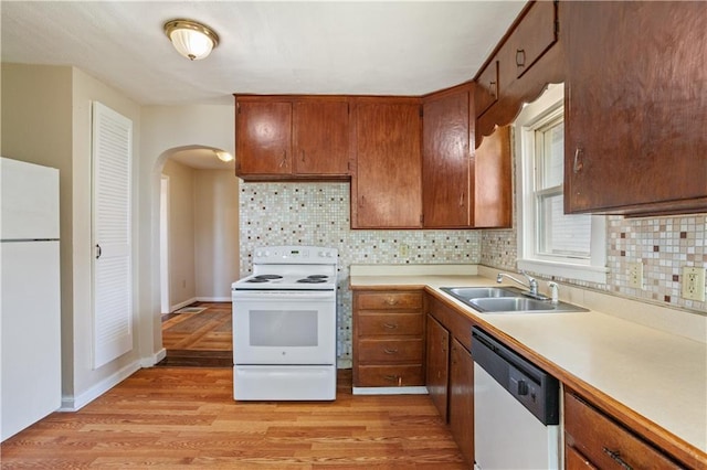 kitchen featuring a sink, white appliances, light wood-style flooring, light countertops, and arched walkways