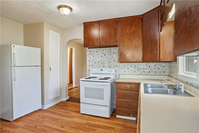 kitchen with white appliances, light wood finished floors, a sink, arched walkways, and light countertops