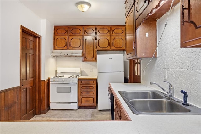 kitchen featuring a sink, brown cabinetry, white appliances, under cabinet range hood, and light countertops