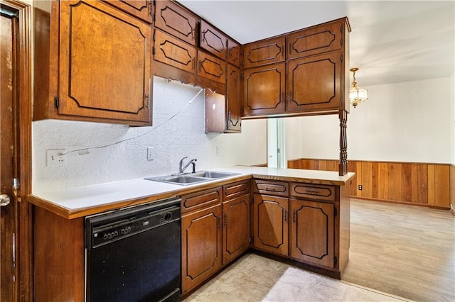 kitchen featuring a peninsula, light countertops, a sink, dishwasher, and wooden walls