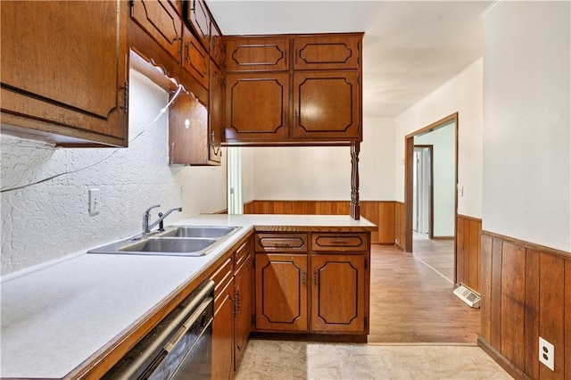kitchen featuring dishwasher, a sink, wooden walls, a wainscoted wall, and light countertops