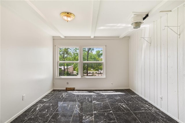 empty room with wood walls, baseboards, and beam ceiling