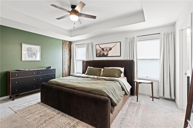 bedroom featuring a tray ceiling, multiple windows, and baseboards