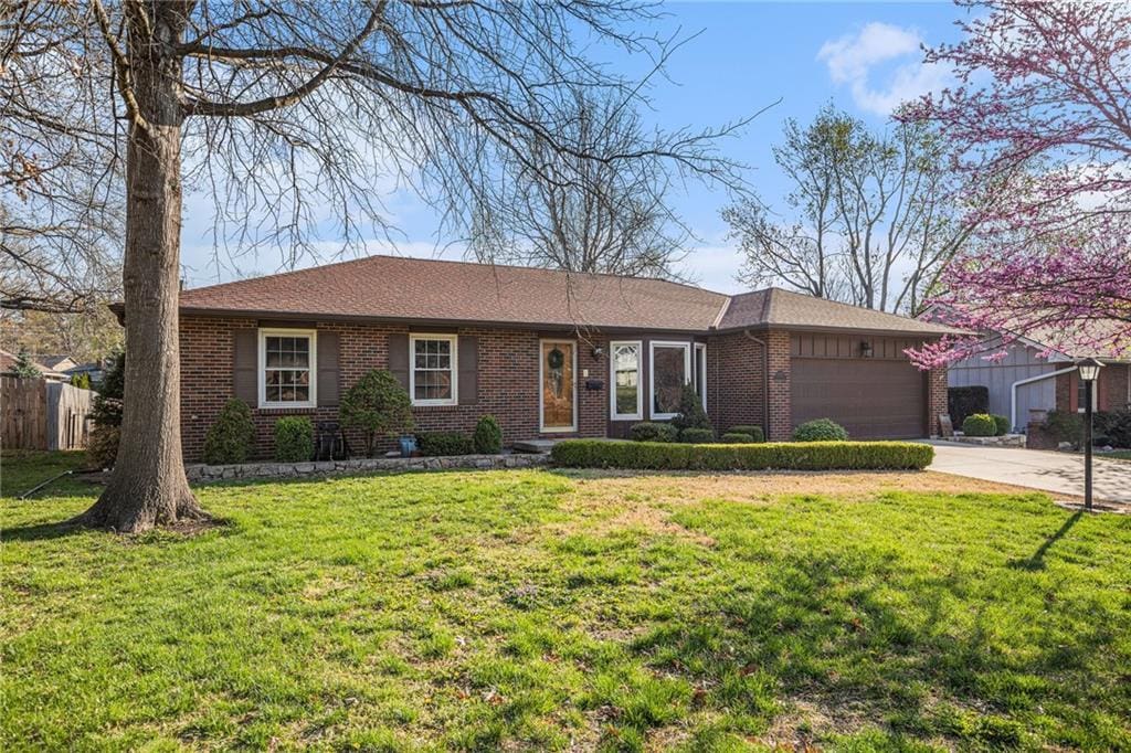 ranch-style home with an attached garage, fence, brick siding, a front lawn, and driveway
