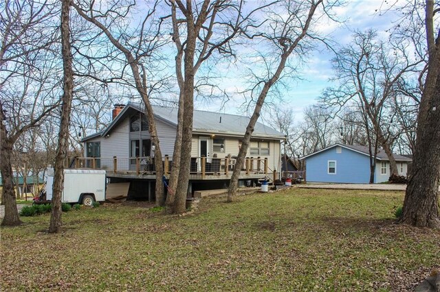rear view of house featuring a wooden deck, a chimney, and a lawn