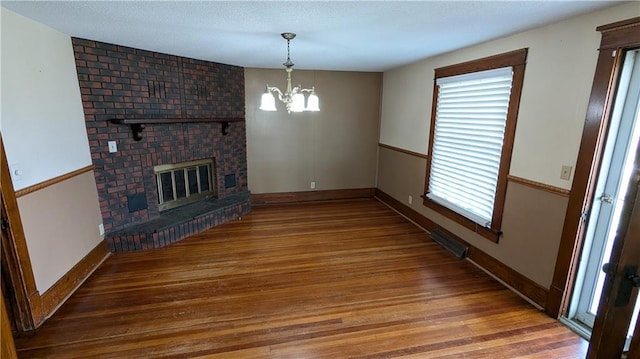 2023 Linden Rd, Hiawatha, KS 66434 - unfurnished living room with visible vents, baseboards, an inviting chandelier, a brick fireplace, and wood finished floors