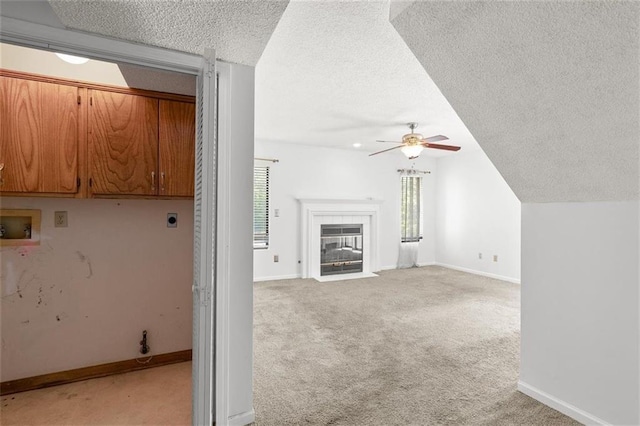 unfurnished living room featuring ceiling fan, a textured ceiling, light carpet, lofted ceiling, and baseboards