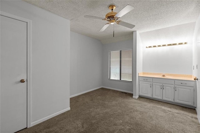 unfurnished bedroom featuring carpet flooring, a textured ceiling, a sink, baseboards, and ceiling fan