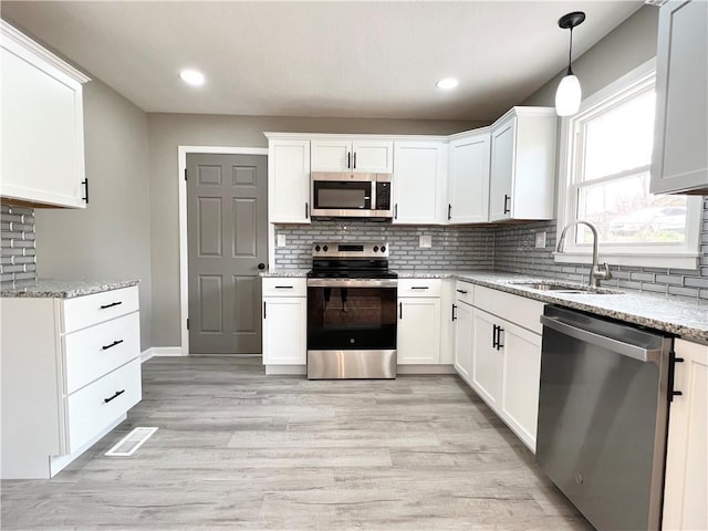 kitchen featuring backsplash, a sink, light stone counters, light wood finished floors, and appliances with stainless steel finishes