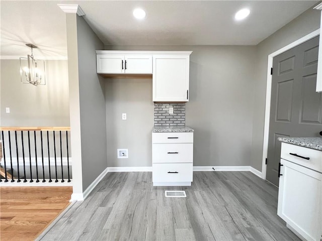 kitchen with light wood-type flooring, white cabinetry, visible vents, and light stone countertops