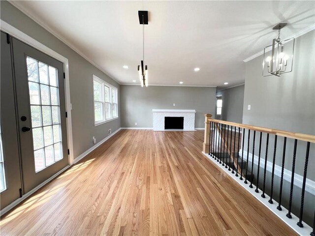 unfurnished living room with crown molding, baseboards, recessed lighting, light wood-type flooring, and a notable chandelier