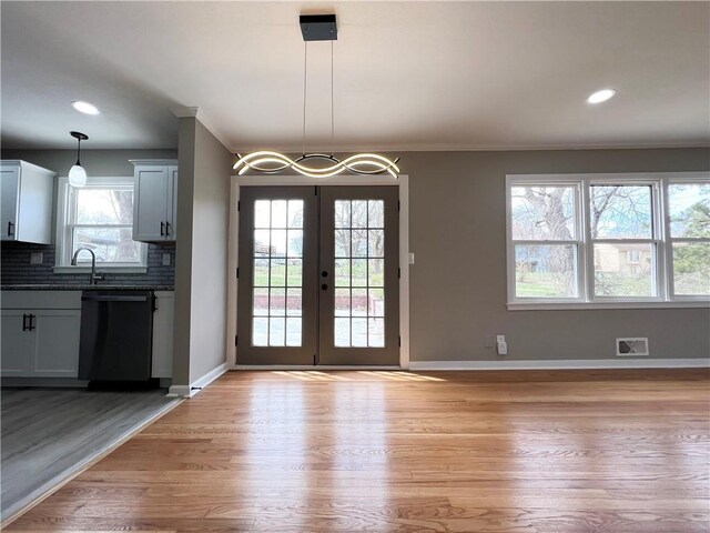 unfurnished dining area with french doors, ornamental molding, baseboards, and light wood finished floors