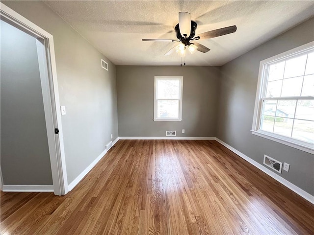 spare room featuring ceiling fan, visible vents, wood finished floors, and plenty of natural light