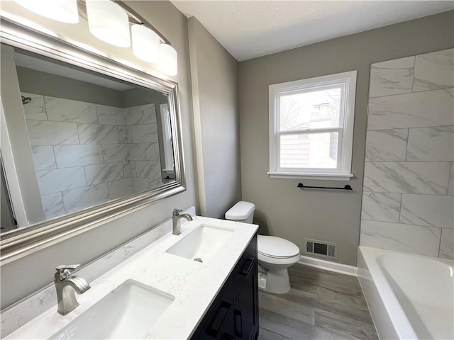 bathroom with toilet, a sink, wood finished floors, and visible vents