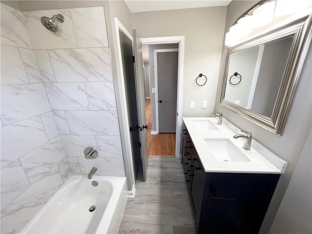 full bath with double vanity, a sink, wood finished floors, and shower / washtub combination
