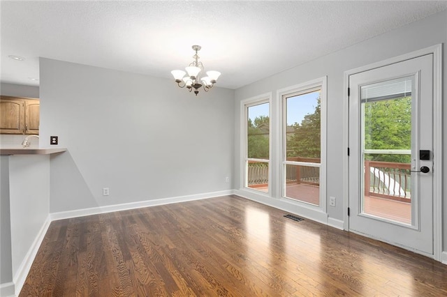 unfurnished dining area with dark wood-style flooring, baseboards, a chandelier, and a healthy amount of sunlight