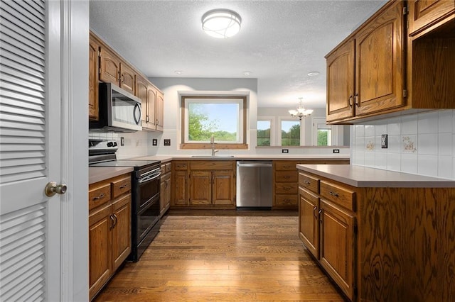 kitchen with brown cabinetry, a sink, appliances with stainless steel finishes, and an inviting chandelier